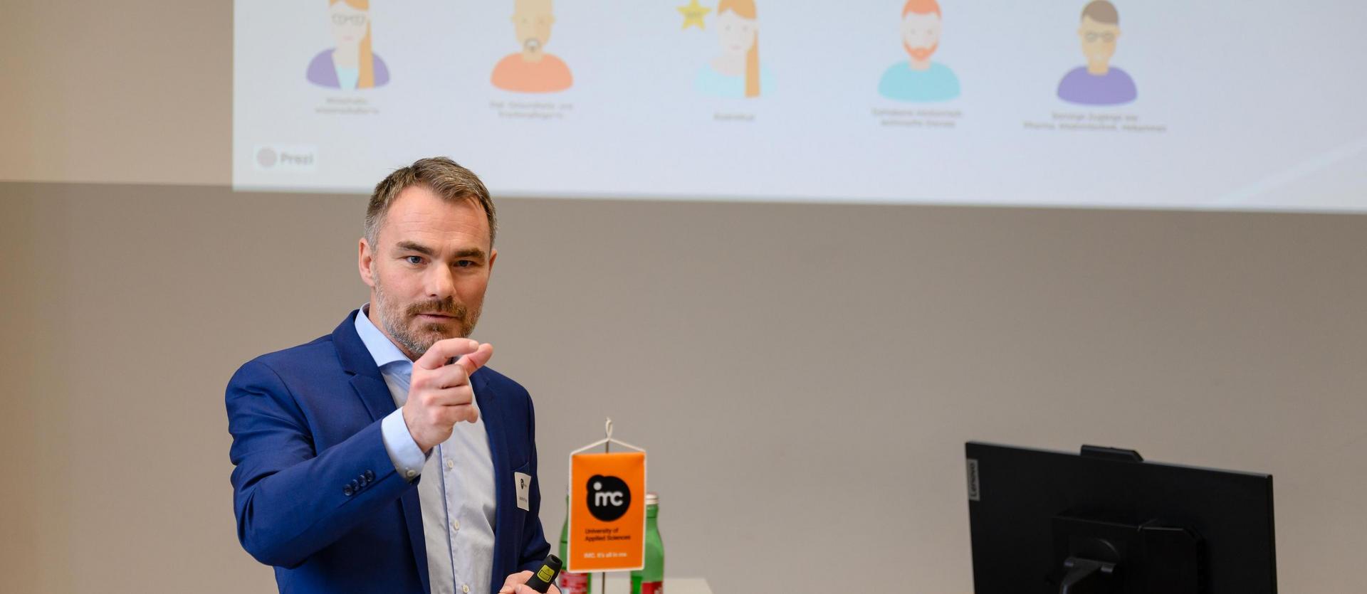Person steht vor einem Publikum und hält eine Präsentation in einem Hörsaal.
